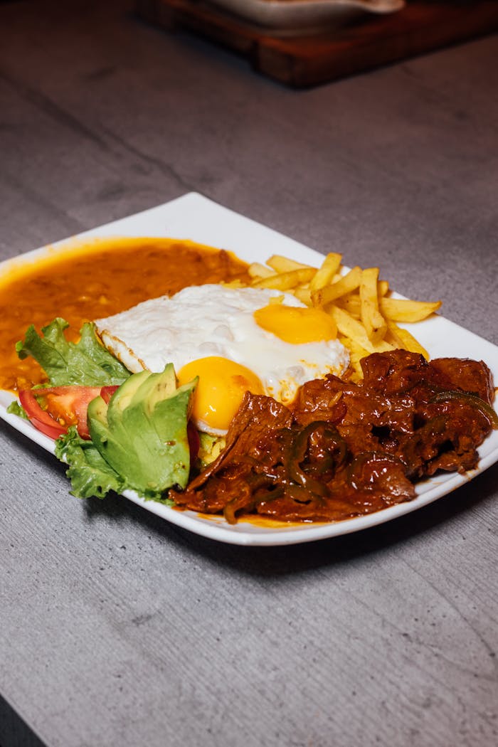 Plate of traditional South American meal with fries, avocado, fried egg, and stew.